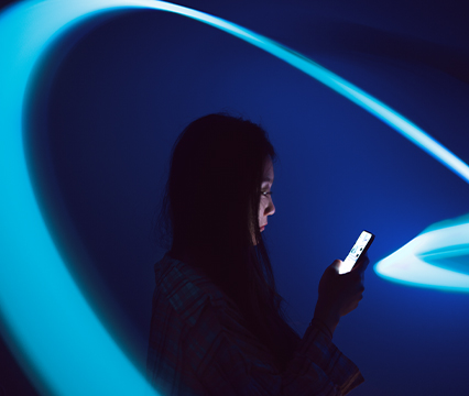 A person looking at a smartphone against a dark blue background with sweeping turquoise light trails.