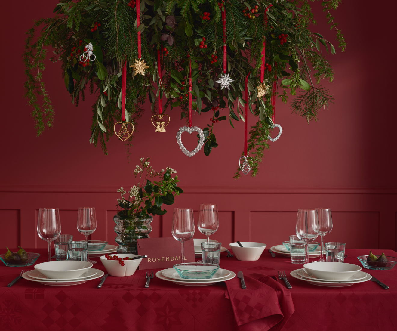 Christmas table setting beneath hanging greenery and gold and silver ornaments.