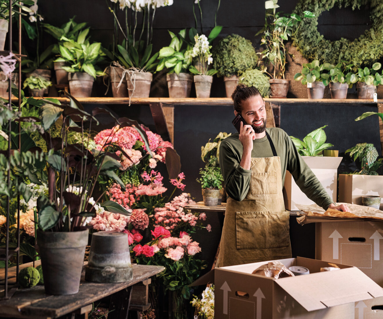 A smiling florist talking on the phone in a shop filled with flowers and plants.