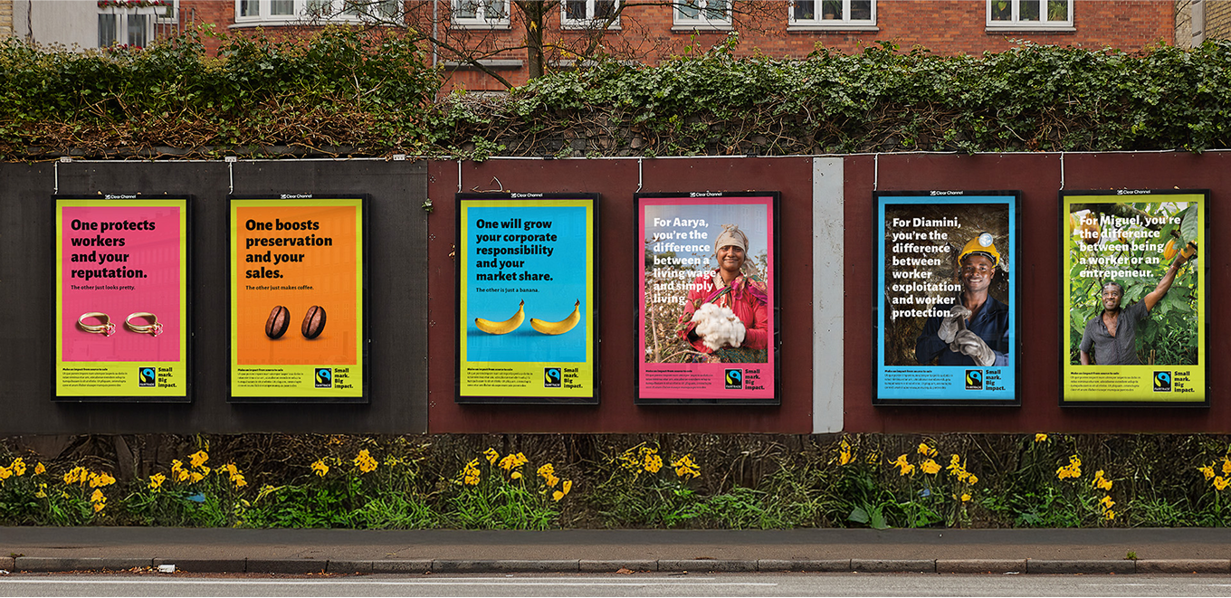 Six colourful Fairtrade campaign posters displayed along a city street, with flowers and greenery in the background.
